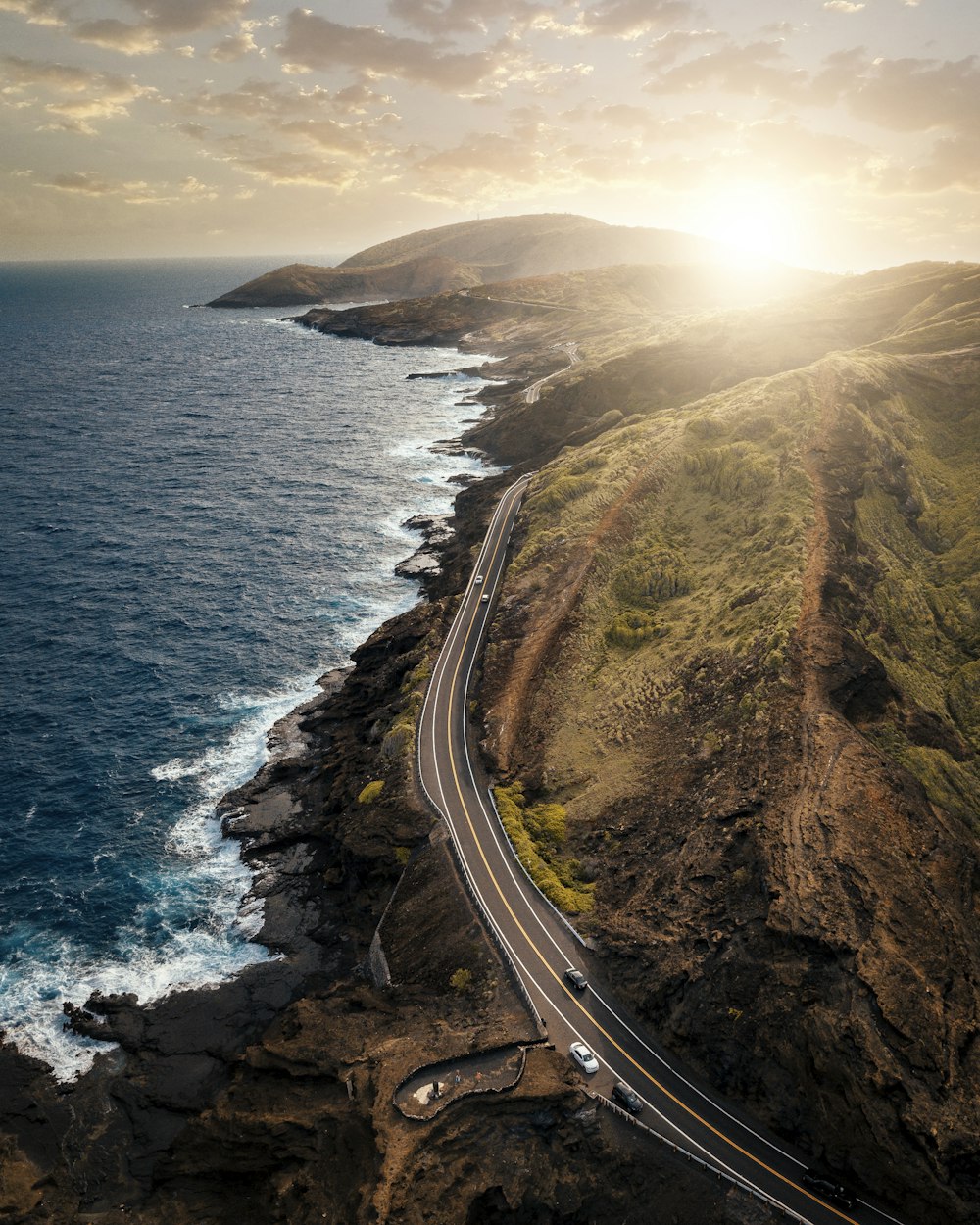 vehicles passing on road beside body of water during daytime