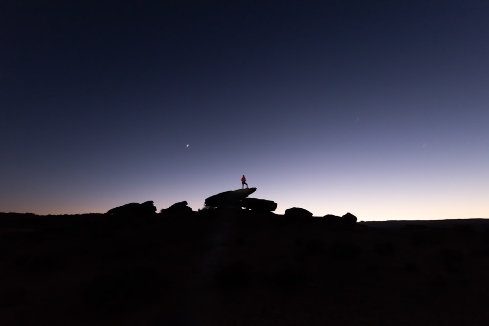 silhouette of person standing on rocks during nighttime
