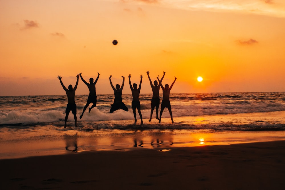 time lapse photography of group of people jumping on seashore under golden hour