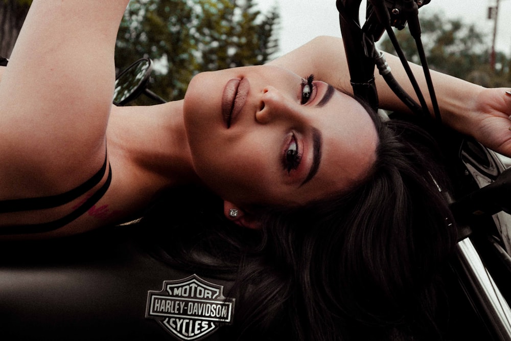 woman lying on black Harley-Davidson motorcycle during daytime
