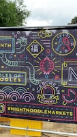 A vibrant banner with neon-style illustrations and text, featuring images of noodles, ice cream, a champagne glass, and various abstract shapes. There is also the hashtag #NIGHTNOODLEMARKETS displayed prominently.