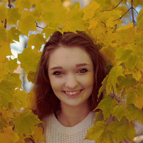 A cheerful woman with silver hair laughing outdoors surrounded by colorful autumn leaves.