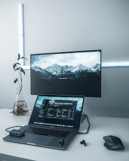 turned-on flat screen TV near MacBook Pro, black wireless earbuds, and black wireless computer mouse on white table