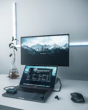 turned-on flat screen TV near MacBook Pro, black wireless earbuds, and black wireless computer mouse on white table