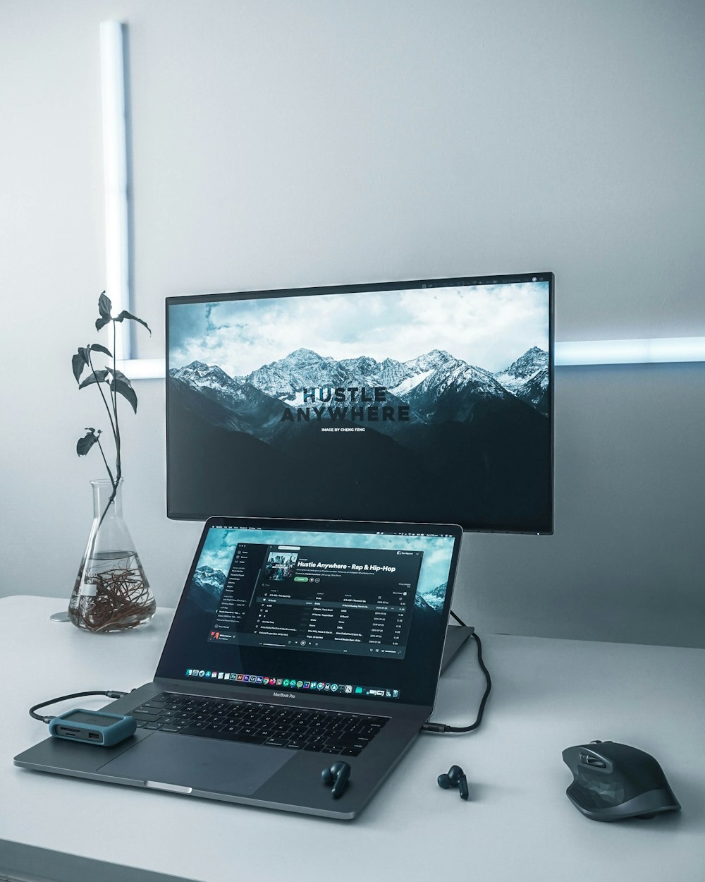 turned-on flat screen TV near MacBook Pro, black wireless earbuds, and black wireless computer mouse on white table