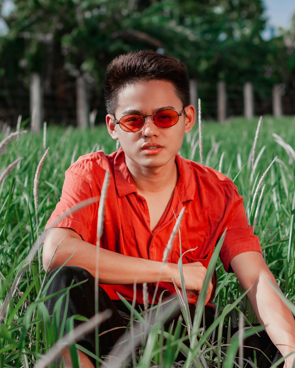 uomo che indossa camicia rossa e occhiali da sole seduto sull'erba