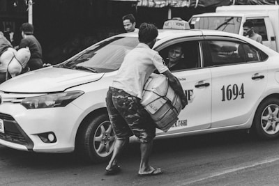A mobile taxi driver assisting a passenger with luggage at a busy street.