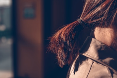 A close-up view of a person's hair tied in a ponytail with a black hair tie. The sunlight casts a warm glow on the brown strands, creating a soft contrast with the shadowed background.
