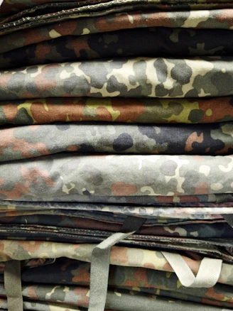 A set of durable camouflage hunting jackets and pants laid out on a wooden bench.