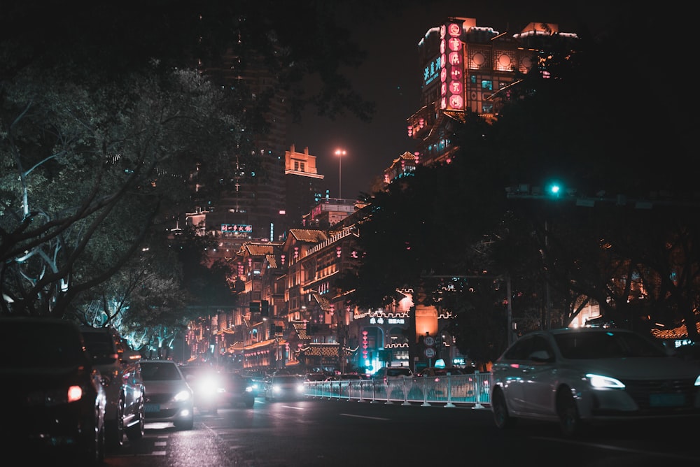 Vehículos en la carretera cerca de árboles y edificios por la noche