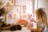 A child interacts with a pink teddy bear on a table adorned with a wooden rainbow and cloud decoration. In the background, there are framed pieces of floral artwork with earthy colors. Natural elements like pine cones and dried flowers in a vase add an organic touch to the scene.