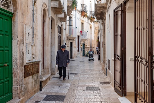 man using walking cane while walking on pathway near buildings during daytime in Locorotondo Italy