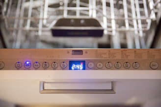 Close-up view of a dishwasher panel with various buttons and a digital display showing the time 2:45. The buttons include options like auto, eco, and different wash cycles. The background shows part of the dishwasher rack.