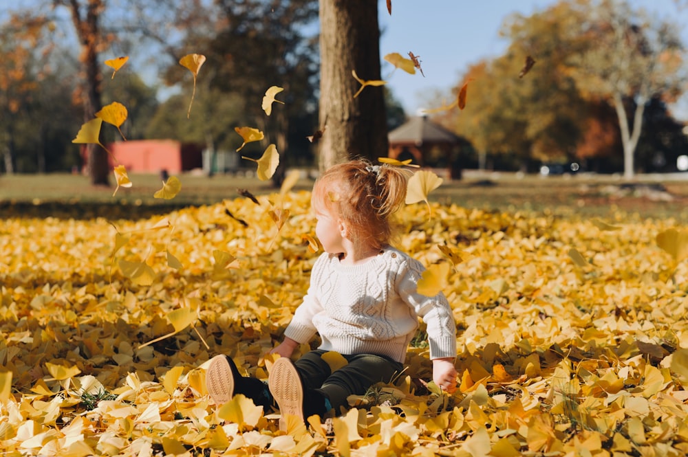 boy's white long-sleeved shirt sitting on withered leaves sitting near tree trunk