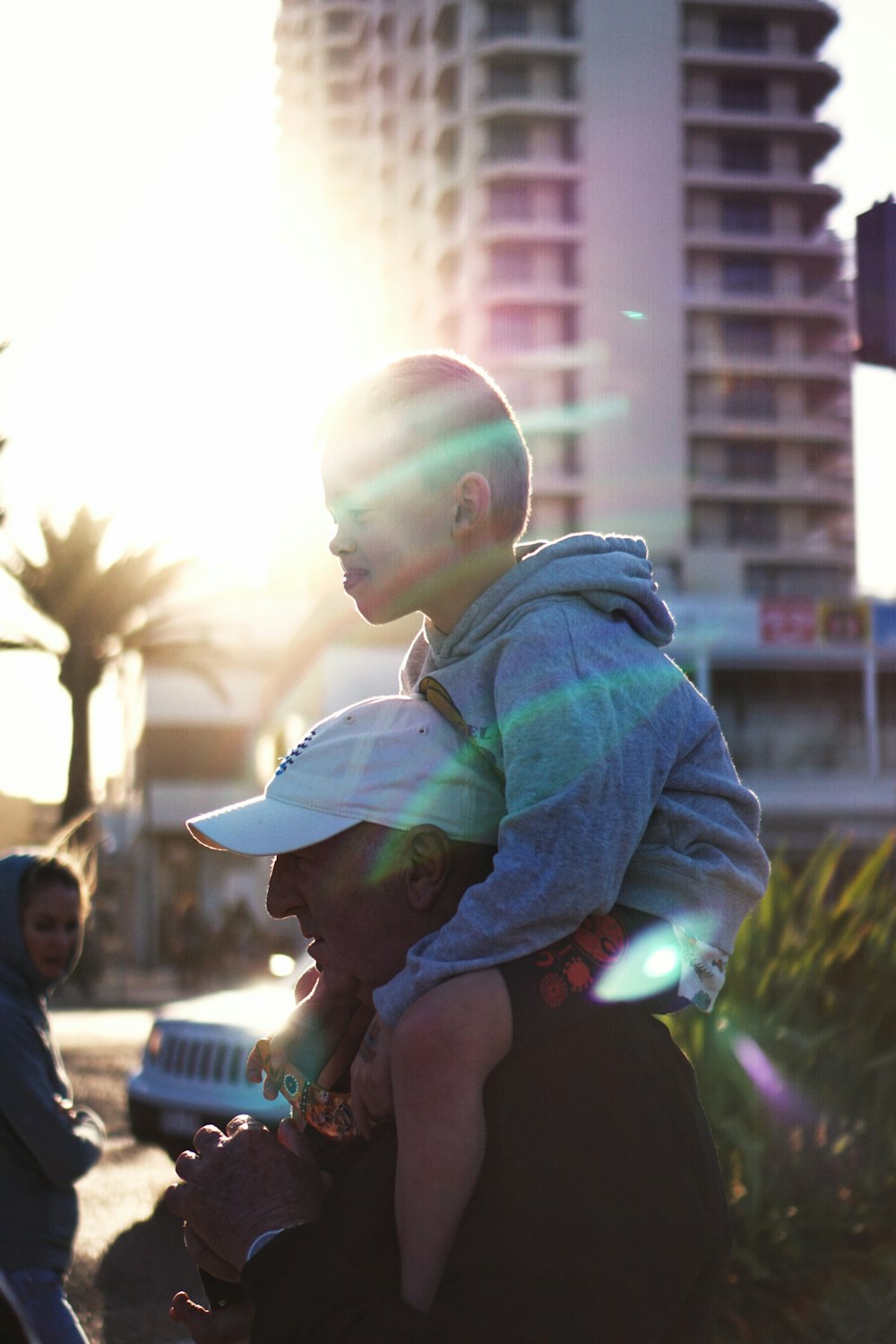 boy wearing grey hoodie riding on man's shoulder