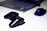 A black gaming console controller is placed on a light surface next to a sleek laptop and a gaming mouse with a blue LED light. The setting suggests a gaming or tech workspace with a focus on modern electronic devices.