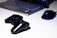 A black gaming console controller is placed on a light surface next to a sleek laptop and a gaming mouse with a blue LED light. The setting suggests a gaming or tech workspace with a focus on modern electronic devices.