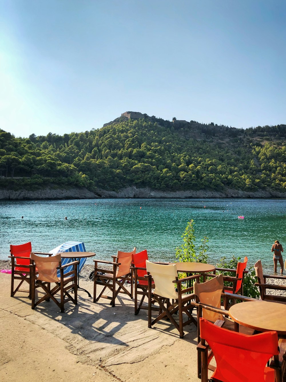 chairs and tables near body of water and mountain