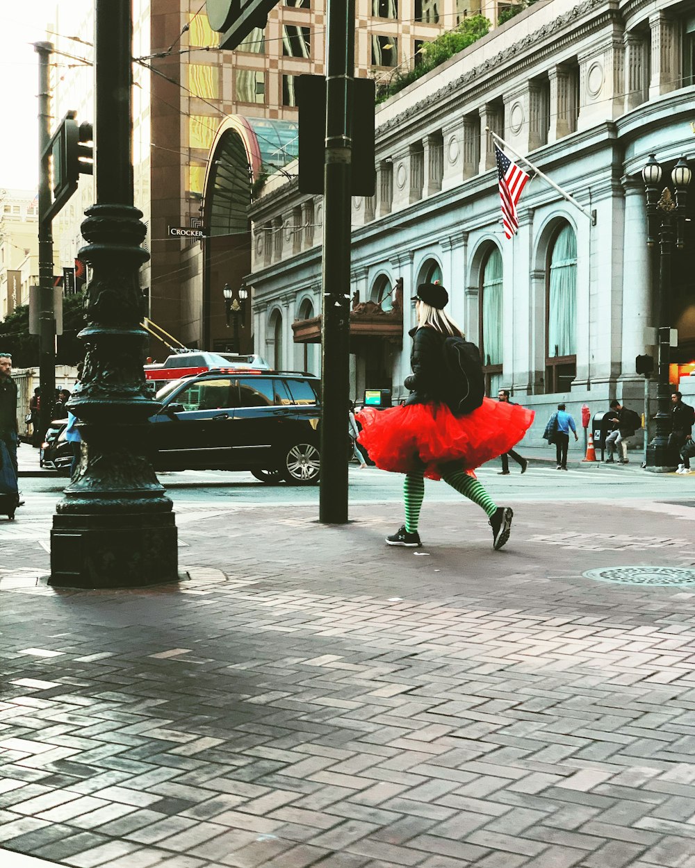 woman wearing black and red tutu skirt walking on sidewalk near street lamp