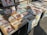 A collection of colorful paintings laid out on a table outdoors, depicting various scenes, including landmarks like the Eiffel Tower and vibrant street views. The paintings are displayed on a light wooden table under natural sunlight.