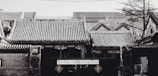 A traditional Chinese building with intricate tiled roofs lightly dusted with snow. The architectural details include ornate carvings and a mix of brick and wood structures. A sign with Chinese characters hangs prominently on the entrance.