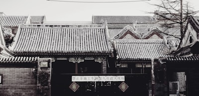 A traditional Chinese building with intricate tiled roofs lightly dusted with snow. The architectural details include ornate carvings and a mix of brick and wood structures. A sign with Chinese characters hangs prominently on the entrance.