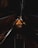 A dimly lit wooden attic space with a high, triangular ceiling supported by exposed beams. A vintage chandelier hangs at the center, casting a warm glow on the wooden surfaces around it.