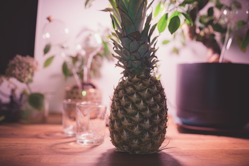 A rustic wooden table displaying fresh pineapples alongside a bottle of Salina's pineapple wine.