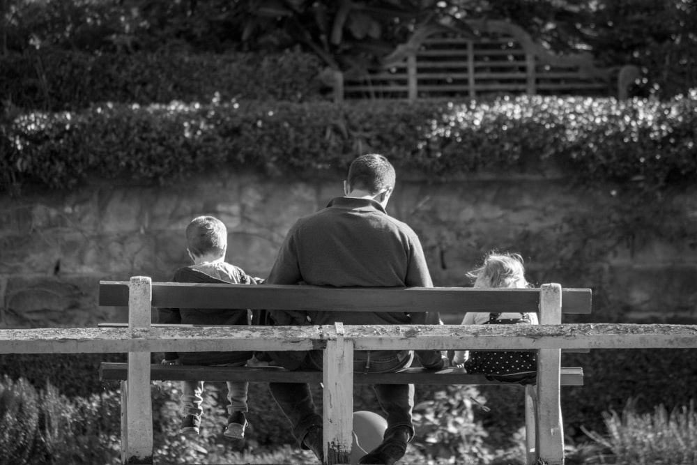 grayscale photography of man and two children sitting in bench