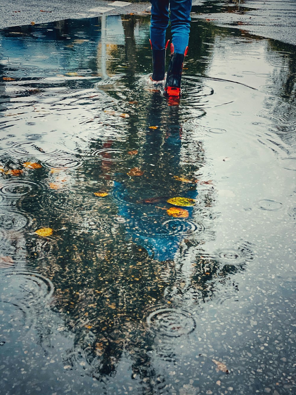 Person mit rot-schwarzen Regenstiefeln, die auf eine Wasserpfütze zugeht