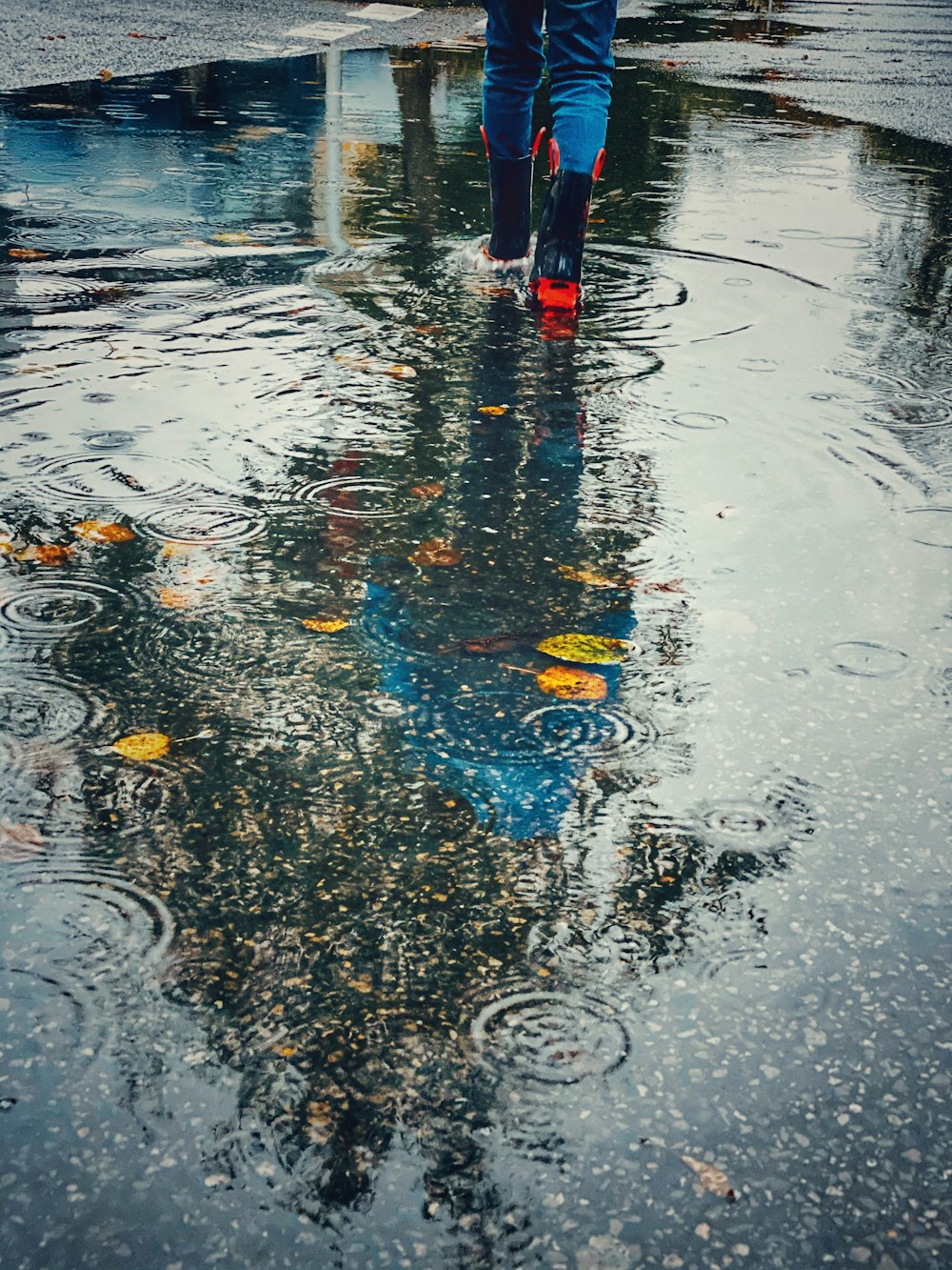 Persona con un par de botas de lluvia rojas y negras caminando hacia el charco de agua