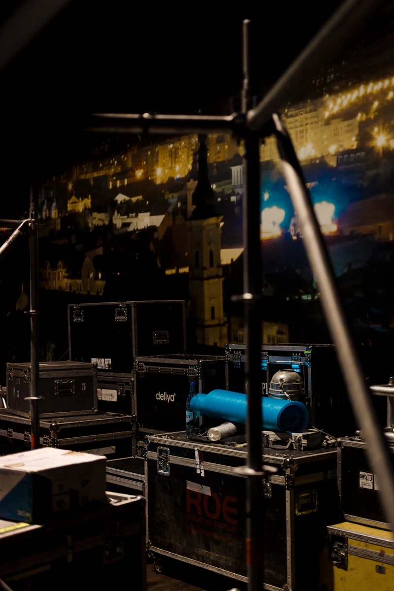 Zwarte flightcases backstage tussen statieven, met het podiumlicht op de achtergrond