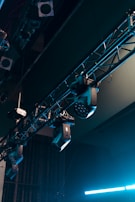 A series of stage lights are attached to a truss structure, with visible cables and metal components. The lights are positioned at various angles, suggesting a setup for a performance or event. The background includes darkened segments, emphasizing the focus on the lighting equipment.