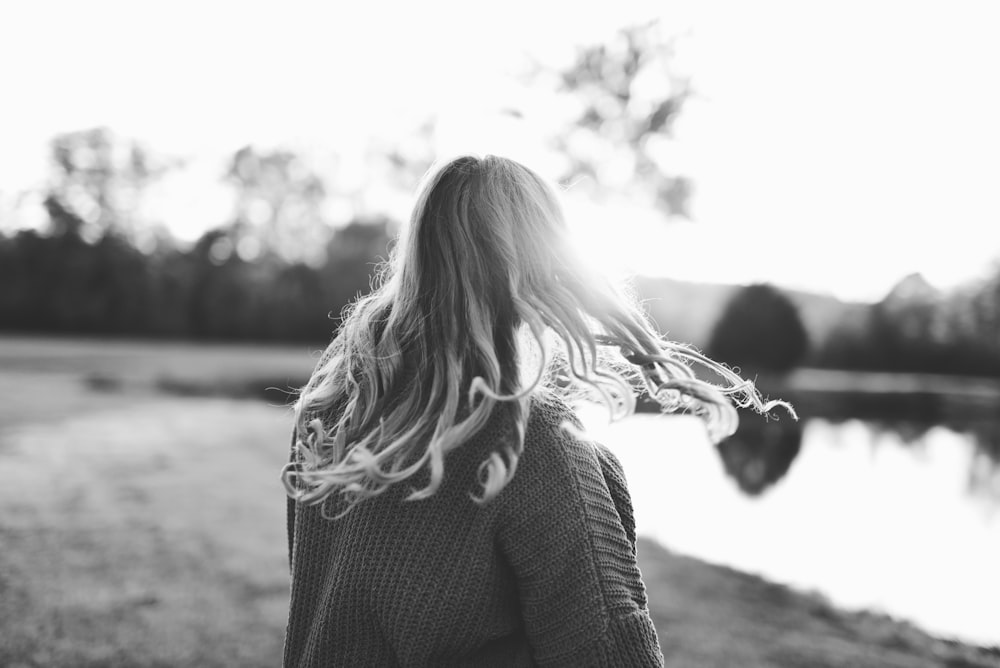 grayscale photography of woman standing in front of body of water