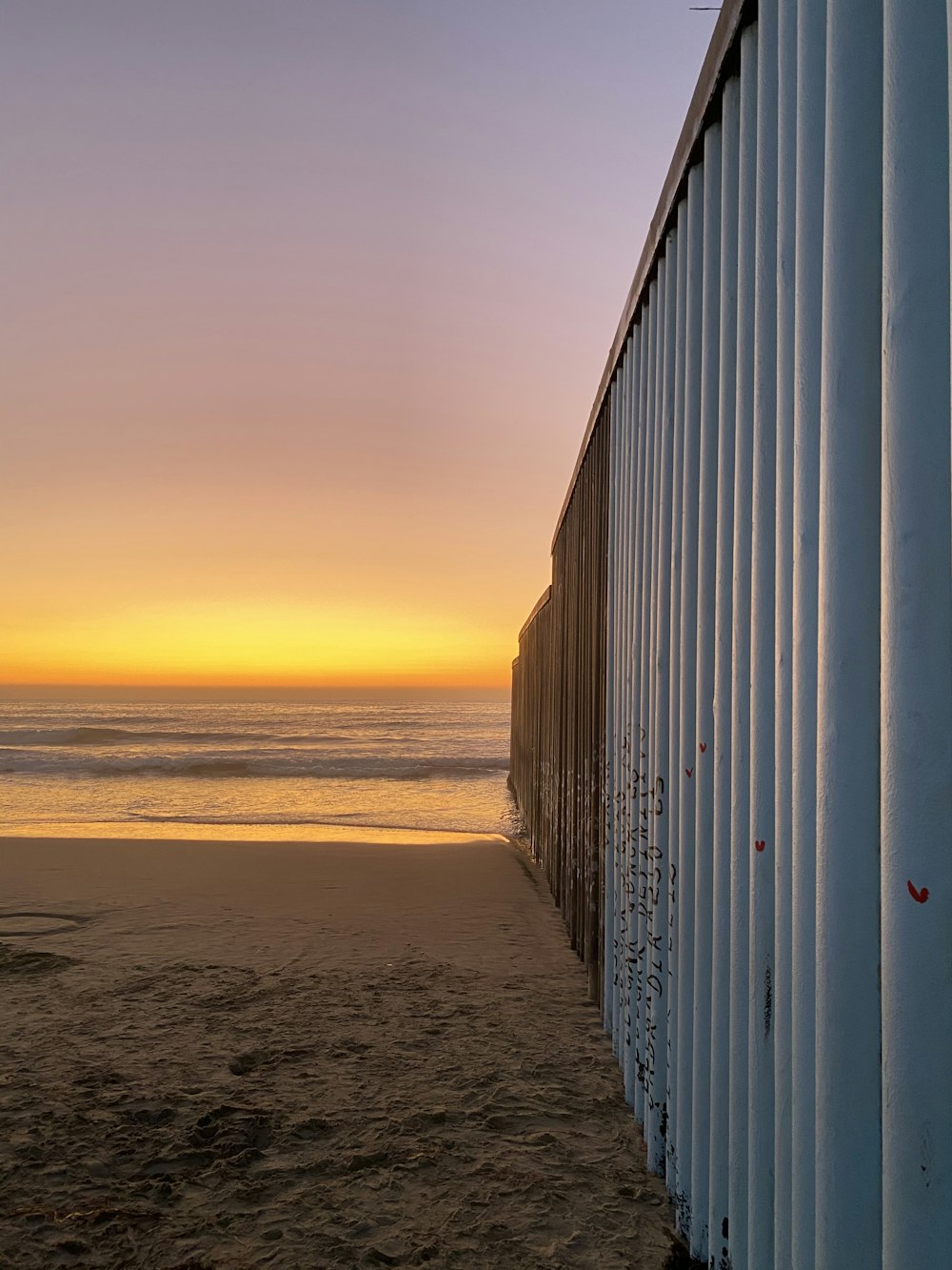 a view of a beach with a fence and a sunset in the background