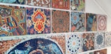 A collection of colorful, intricately designed mosaic tiles arranged on a wall. Each tile displays a distinct geometric or floral pattern, rich in detail and vibrant in colors, showcasing artistic craftsmanship.