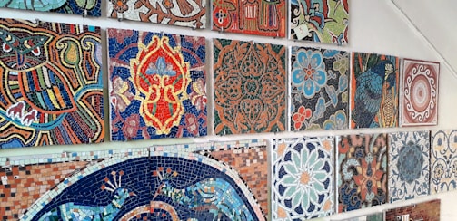 A collection of colorful, intricately designed mosaic tiles arranged on a wall. Each tile displays a distinct geometric or floral pattern, rich in detail and vibrant in colors, showcasing artistic craftsmanship.