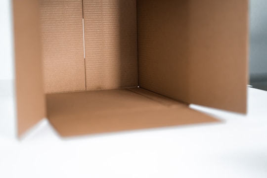 An open cardboard box with light brown corrugated sides and a smooth interior, placed on a white surface with soft natural light coming from the right.