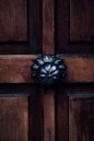 A wooden door with a prominent dark metal decorative knob centrally positioned. The wood features visible grain patterns, adding texture and warmth to the appearance.