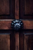 A wooden door with a prominent dark metal decorative knob centrally positioned. The wood features visible grain patterns, adding texture and warmth to the appearance.