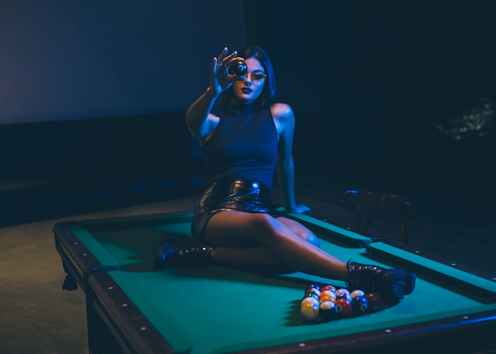 woman sitting on top of a pool table