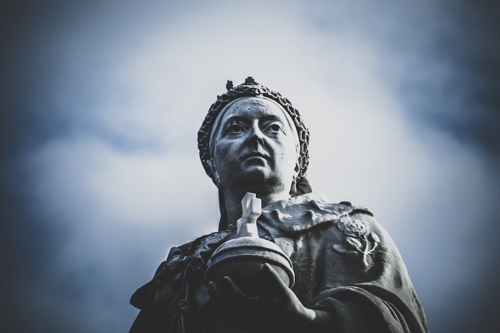 Photographie en contre-plongée d’une femme tenant une statue de croix sous un ciel blanc et bleu pendant la journée