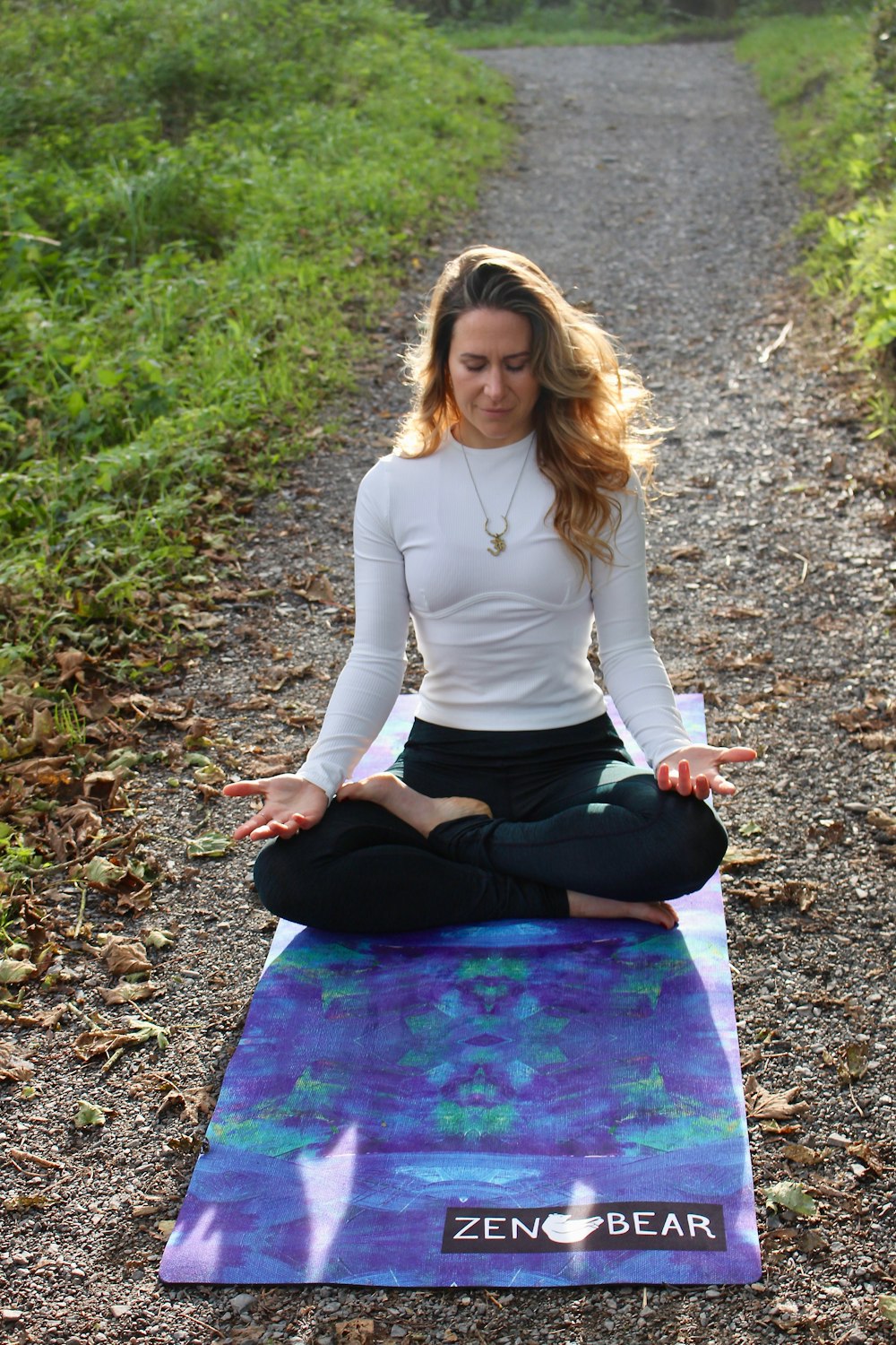 woman meditating on dirt pathway with blue Yoga mat