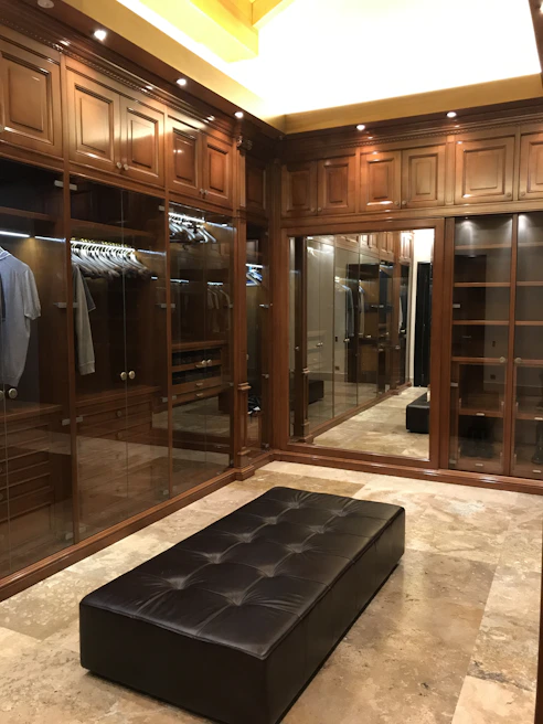 Elegant walk-in closet featuring built-in wardrobes with gold accents and dark wood finishes