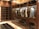 A luxurious walk-in closet with wooden cabinetry and glass doors showcases a neatly organized collection of clothes on hangers. Various shirts and jackets are arranged by color, and shoes are displayed on lower shelves. The warm lighting highlights the richness of the wood.