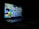 A laptop is positioned in the foreground with its screen displaying colorful graffiti art on a brick wall, featuring abstract and cartoonish characters with vivid expressions. The surroundings are dimly lit, focusing attention on the vibrant screen. The image has a dark, moody ambiance with sharp contrasts between the bright display and the shadowy environment.