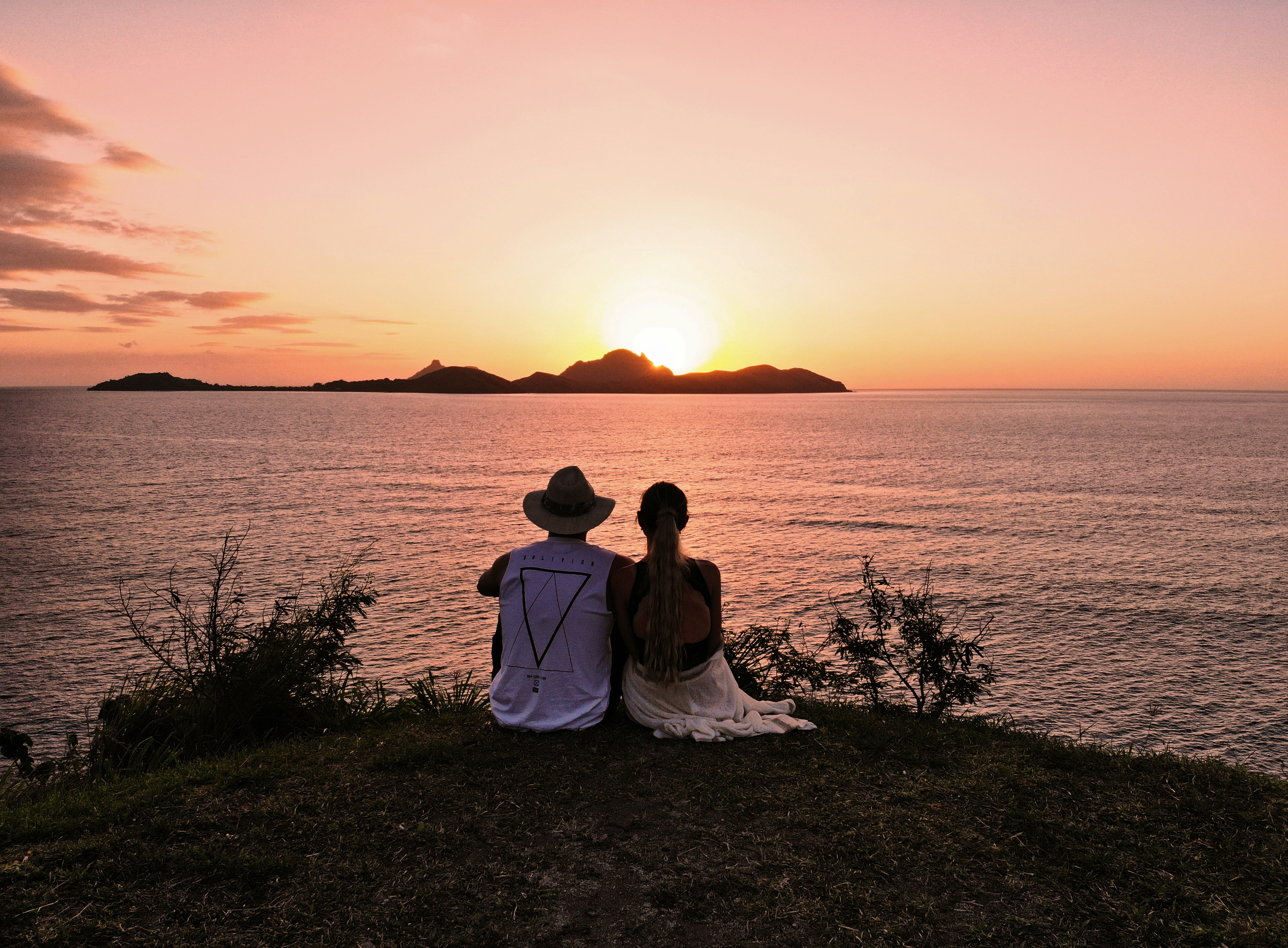 man and woman wearing on grass field looking at sunset behind og silhouette mountain fiji teams background