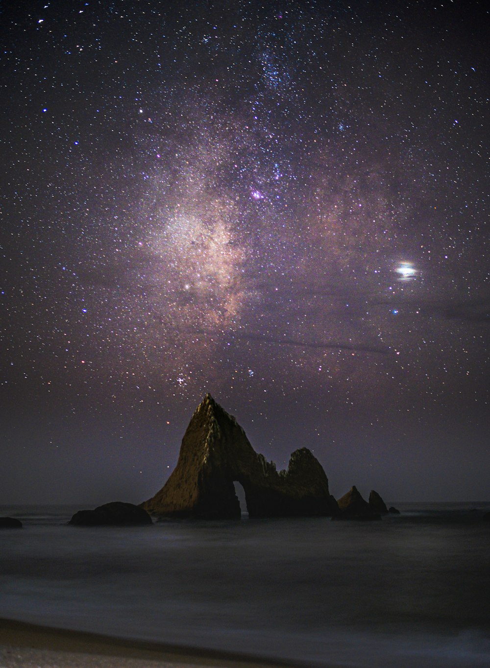 rock formation in water under purple skies