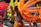 Individuals wearing colorful costumes and elaborate balloon decorations participate in a lively parade. Brightly colored balloons in shades of orange, red, yellow, green, and blue are attached to their outfits, resembling wings or abstract designs. The participants are dressed in festive attire, including tutus and floral headbands, with some on roller skates.