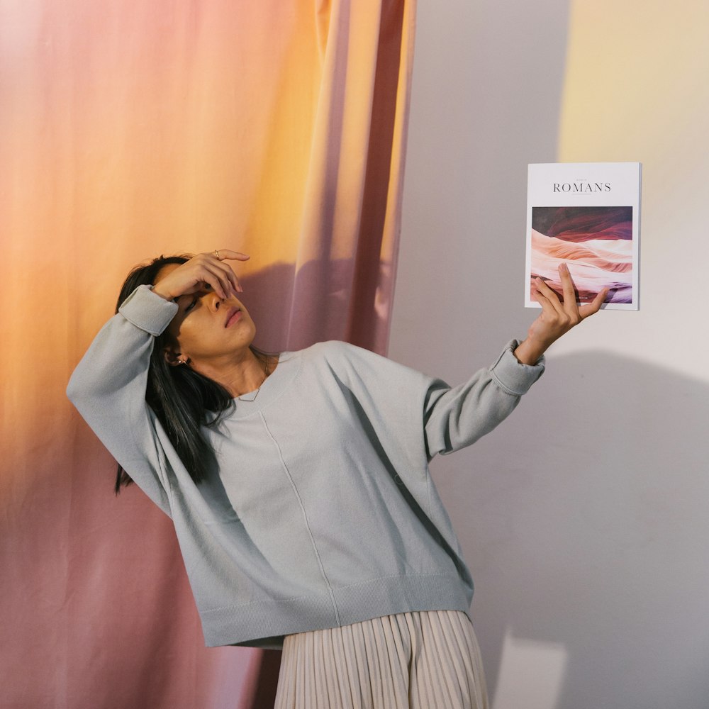 shallow focus photo of woman in gray crew-neck long-sleeved holding book